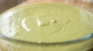 "Pistachio-colored cake batter being mixed in a bowl, showcasing a smooth, aerated consistency after adding eggs and extracts."