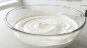 A glass bowl containing a perfectly smooth and creamy mixture of whipped cream cheese and sugar, prepared as the filling for a no-bake mango cheesecake.