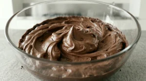 A glass bowl filled with perfectly whipped, light, and fluffy chocolate frosting with soft peaks, ready to be spread onto cake layers.