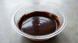 "A glass bowl containing a rich, smooth chocolate batter after whisking in olive oil, eggs, vanilla, and warm water."
