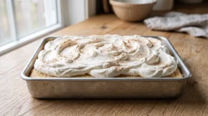 Tres Leches cake in a pan topped with an even layer of freshly whipped cream and a dusting of cinnamon.