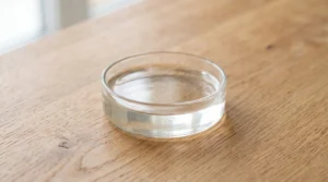 A small glass dish containing clear cold water on a wooden countertop.