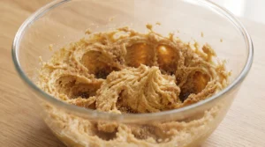 A glass bowl containing creamed butter and brown sugar mixture on a wooden countertop