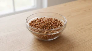 A glass bowl filled with freshly chopped toasted pecans on a wooden countertop.